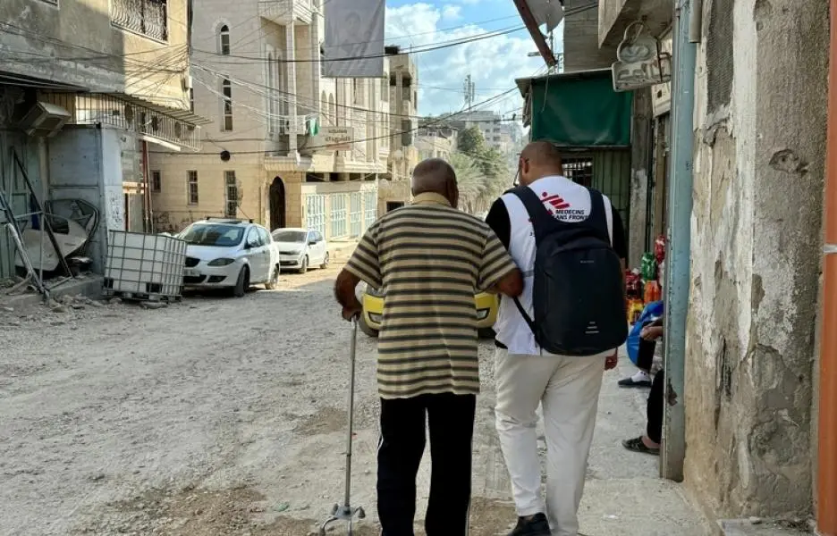 Un miembro del equipo de MSF ayuda a caminar a un adulto mayor en el campo de Tulkarem, Cisjordania (Territorios Palestinos Ocupados).