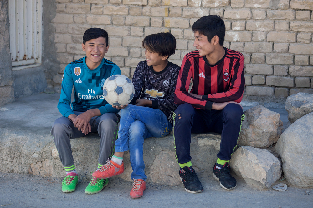 Ali Sina, de 13 años, se sienta con su hermano y su amigo en la calle cerca de su casa donde juega al fútbol en Hazara Town, Quetta, Pakistán.