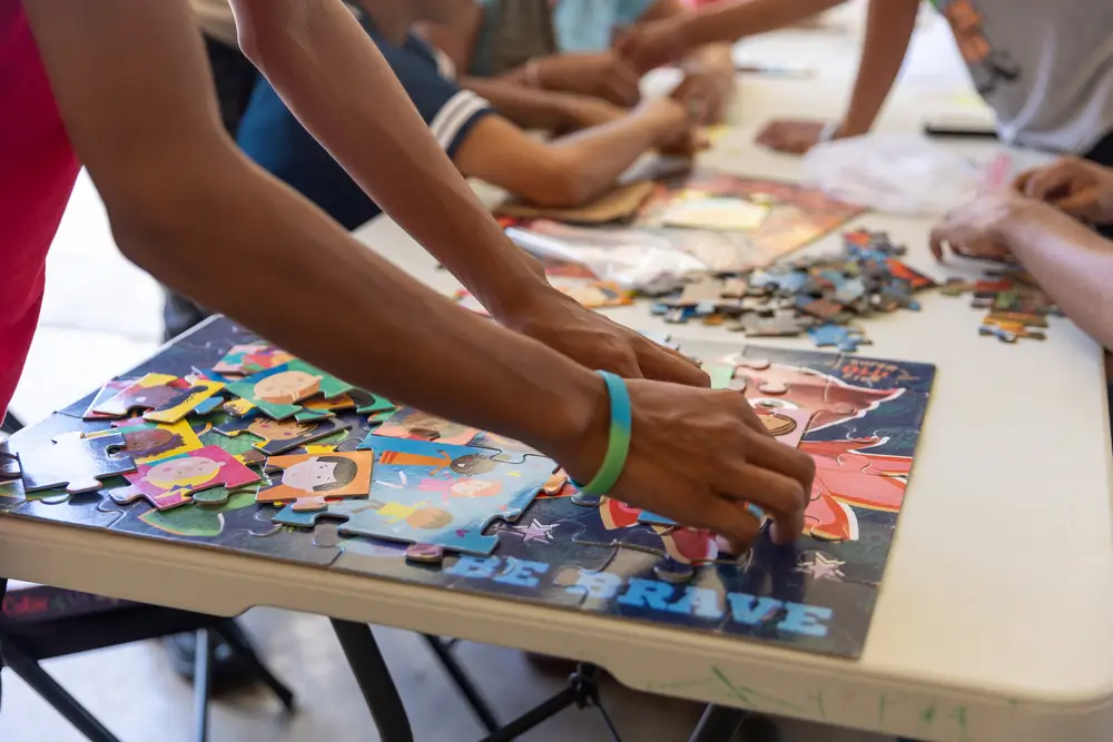 Niños y jóvenes migrantes juegan con un rompecabezas en la Casa del Migrante de Reynosa, Tamaulipas. México 2024. 