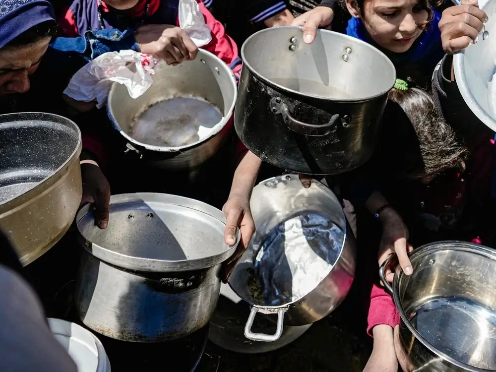 Niños y niñas sostienen sus ollas vacías en una cocina comunitaria en el norte de Gaza, Palestina, febrero de 2025.