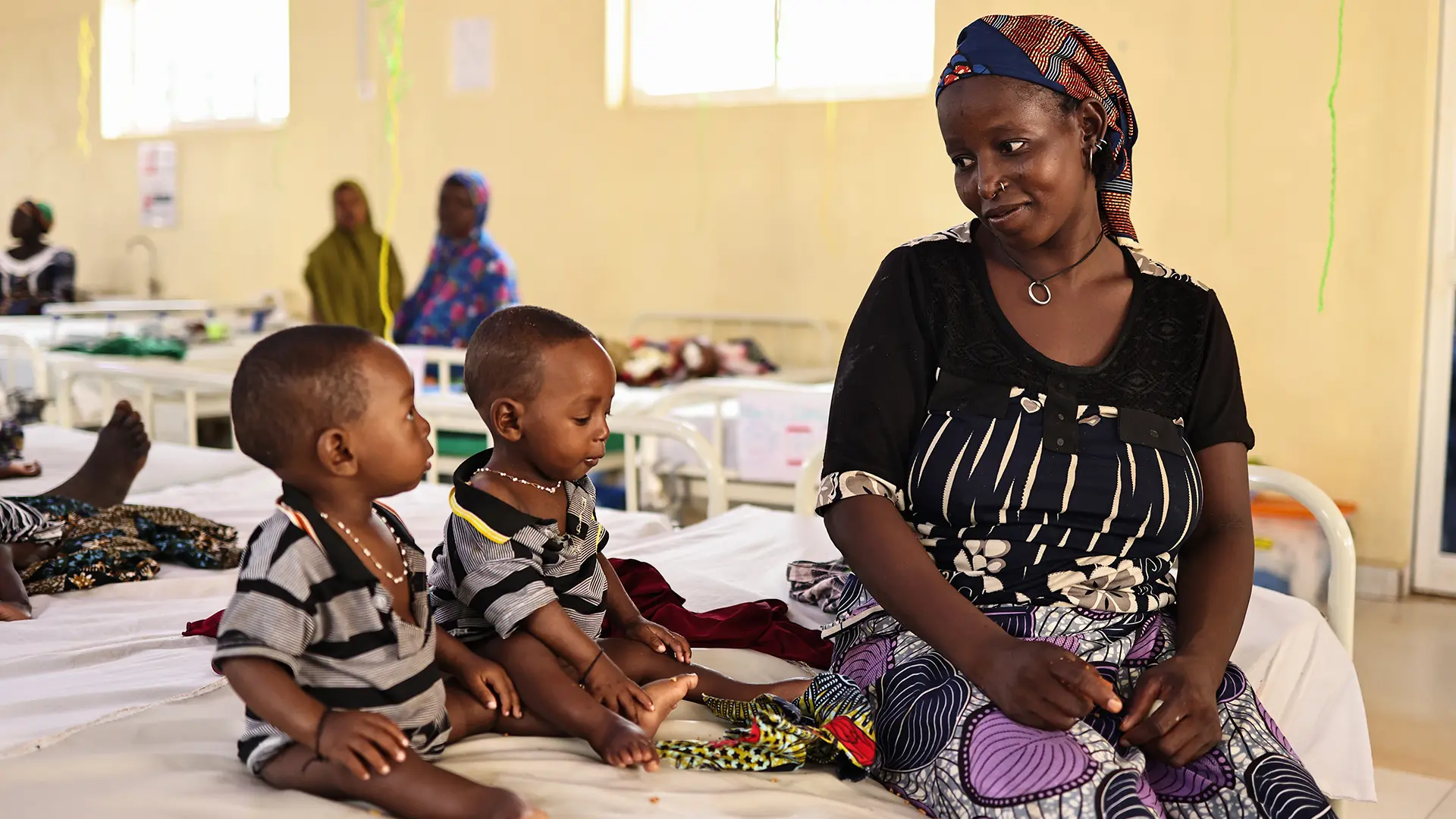 Binta Abdulraziqu junto a sus hijos gemelos, quienes fueron ingresados ​​por desnutrición aguda grave en el centro de nutrición terapéutica para pacientes hospitalizados de Maiyama. Estado de Kebbi, Nigeria, agosto de 2025.