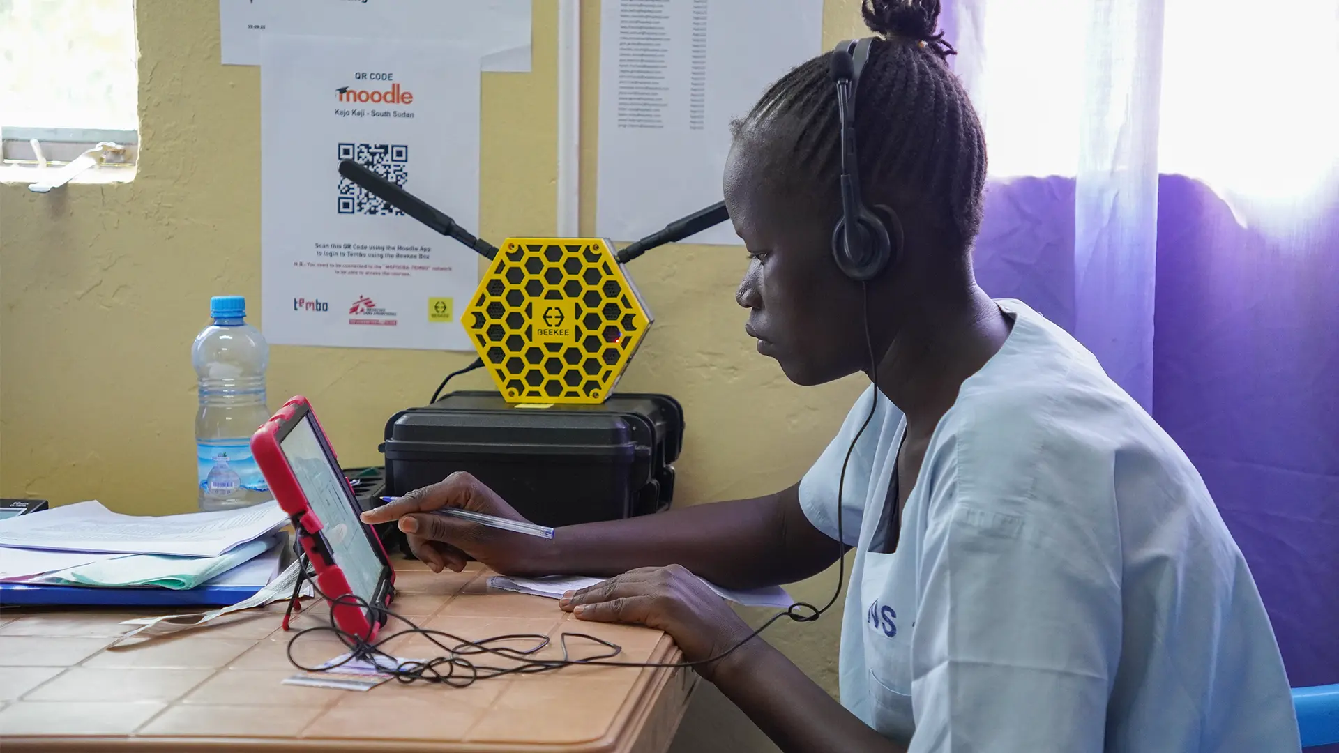 Una enfermera utiliza una tableta para acceder al contenido de aprendizaje electrónico del programa de capacitación y ponerse al día con las sesiones perdidas, directamente en el aula de la Academia MSF del hospital. Al fondo, el «Beekee Hub», un sistema implementado con el apoyo de Tembo como parte de su proyecto de accesibilidad sobre el terreno, permite a los alumnos acceder al contenido de aprendizaje electrónico sin necesidad de conexión a Internet.