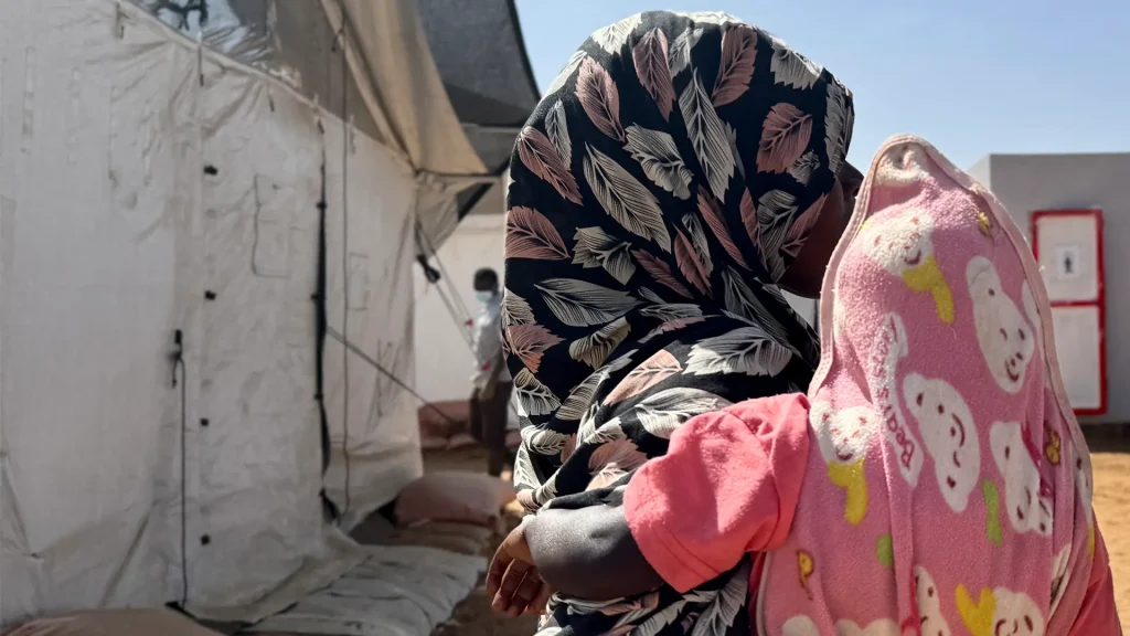 Amina* abraza a un niño frente a un refugio improvisado en Tawila. Mientras huía de El Fasher con sus hijos, fue violada por hombres armados. Estado de Darfur del Norte, Sudán, febrero de 2026. *Se ha utilizado un seudónimo para proteger su identidad.