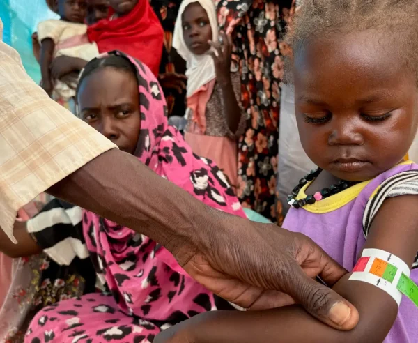 Un miembro del personal de MSF mide la circunferencia media del brazo (CMB) de Nouran Abdallah, de 2 años, quien huyó de El Fasher el 11 de octubre con su familia. La medición muestra desnutrición aguda moderada; será inscrita en el programa de la Clínica de Desnutrición Aguda Moderada en el campamento de desplazados de Dabaniera.