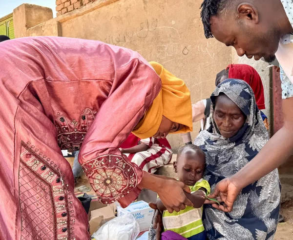 Un voluntario comunitario y un miembro del personal de MSF realizan un cribado MUAC, en Mohamed Ayoub, de 18 meses, inmediatamente después de su vacunación contra el sarampión.