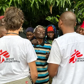 El personal de MSF Nathalie Gielen y Gimo Lazimo hablan con un grupo de personas desplazadas que esperan fuera de una clínica móvil de MSF en Alua Velha, distrito de Eráti, provincia de Nampula.